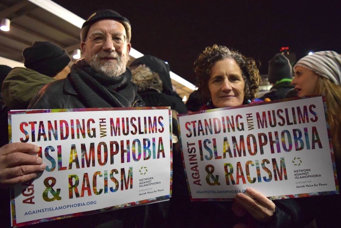 Two protestors at JFK International Airport with signs reading "Standing with Muslims Against Islamophobia and Racism".