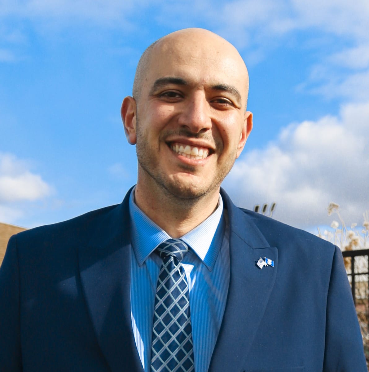A portrait of a bald man smiling and wearing a blue suit.