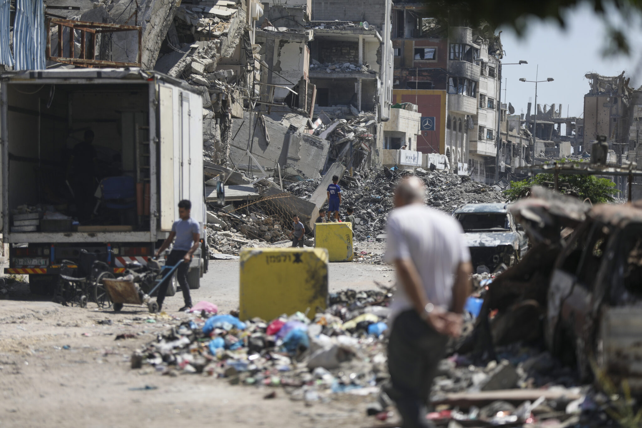 Palestinians walk along a debris-strewn street in the Tuffah neighbourhood of Gaza City, next to yellow concrete blocks marking the 'Yellow Line' imposed by Israel, 27 July 2026. Photo: Yousef Zaanoun