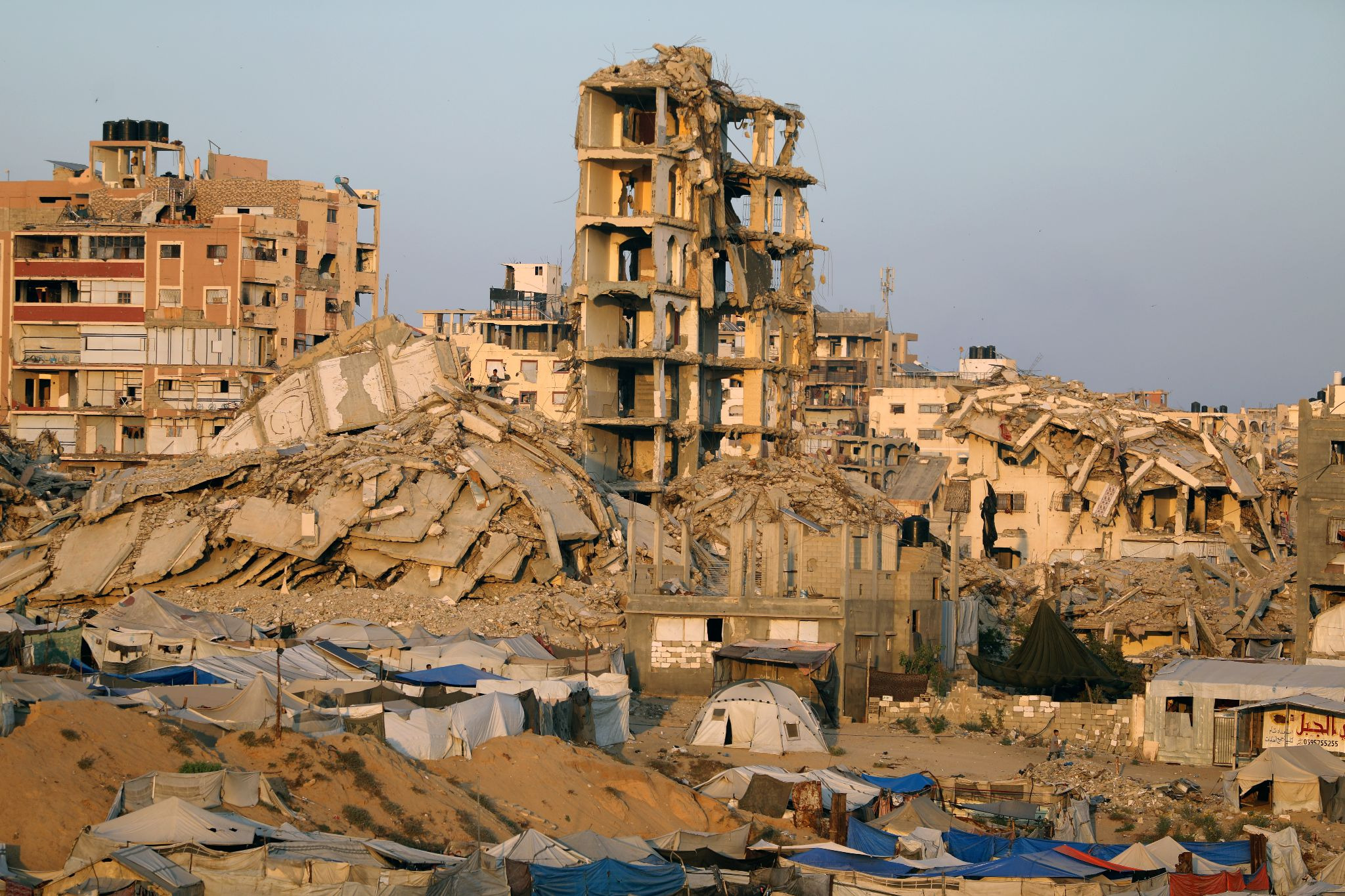 A tent city with a large expanse of destroyed buildings in background.