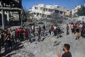 A group of people walk away from collapsing buildings.