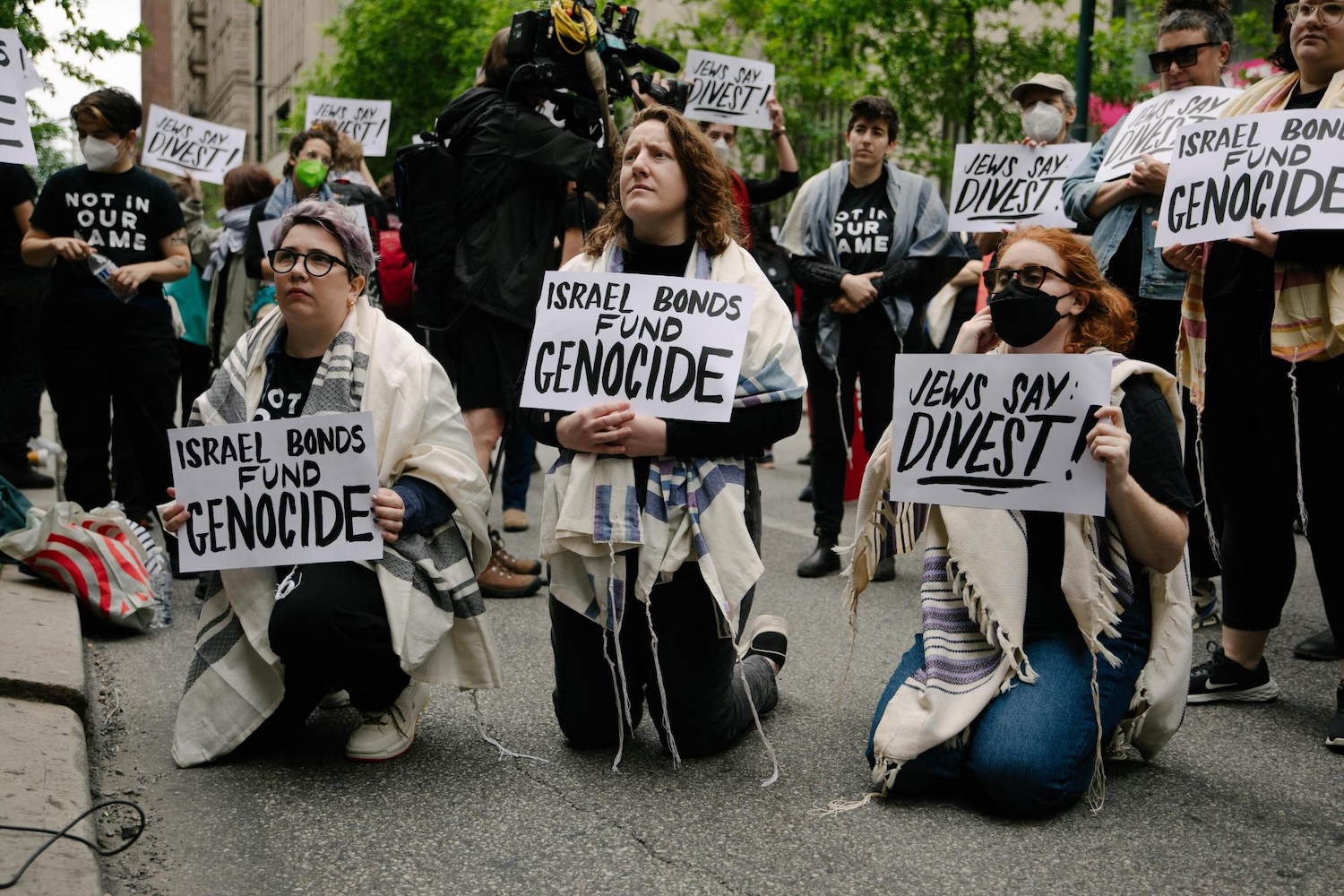signal-2026-09-17-10-59-32-965 A group of people kneel while holding signs that say "Israel Bonds Fund Genocide."