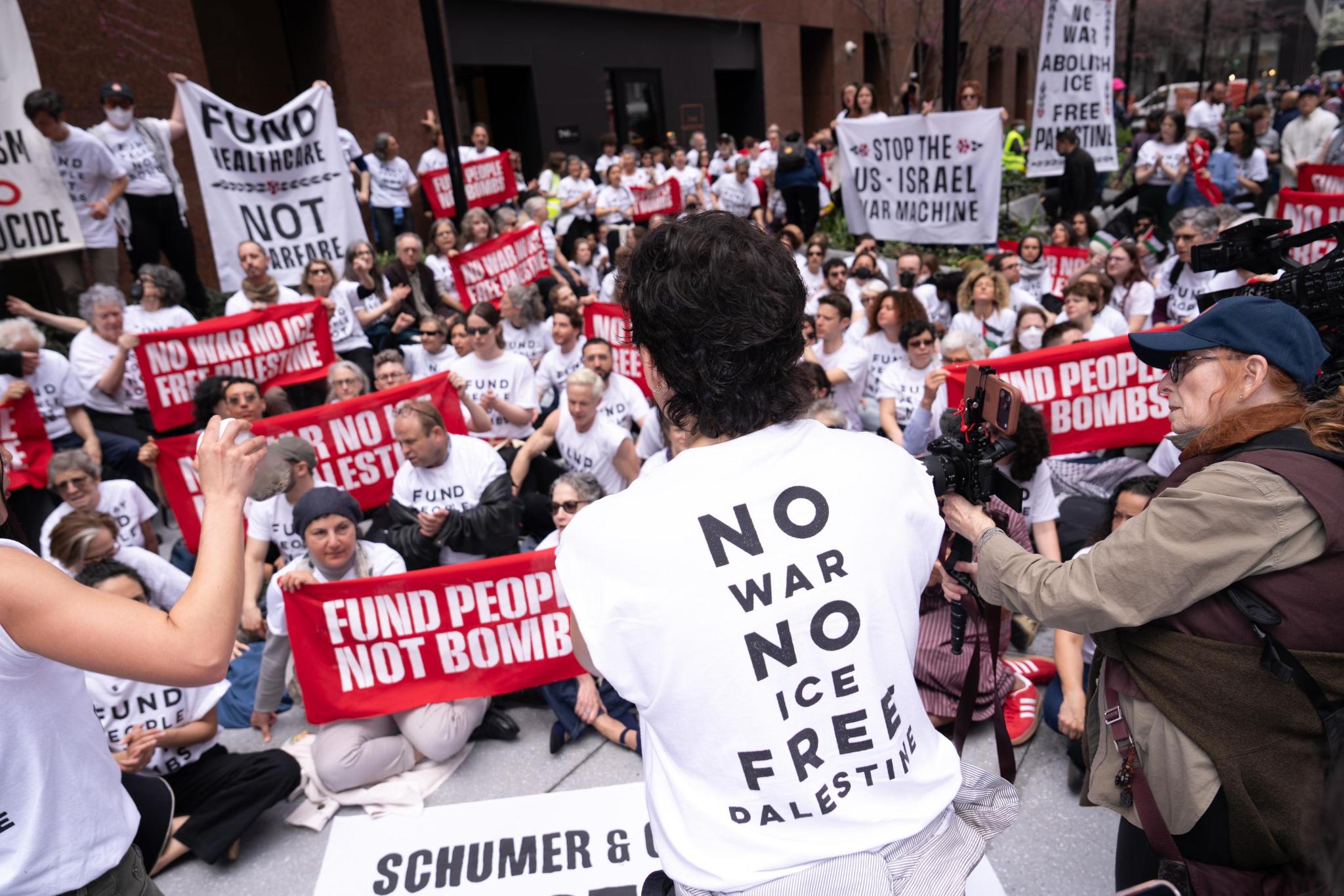 A group of people gather around a person wearing a shirt that says "NO WAR NO ICE FREE PALESTINE"
