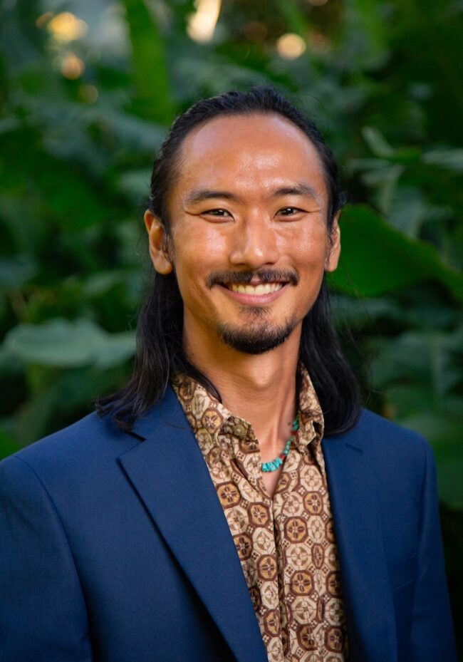 Portrait of a man with long hair smiling in a suit.